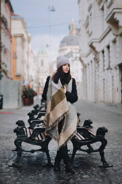 a young girl in coat, angora hat, wide scarf is standing alone leaning on a cast-iron bench awaiting a date. lviv, ukraine. - eyes narrowed imagens e fotografias de stock