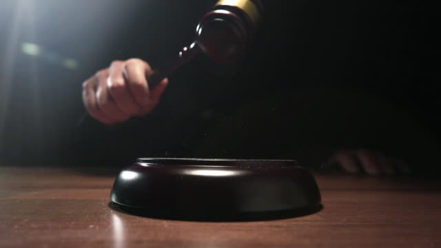 Judge hitting Gavel off a block in courtroom, dark background slow motion dolly shot