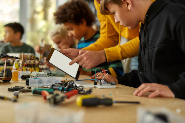 istock Sharing ideas. Cropped shot of young technicians working with a wiring kit at a stem robotics class. Male teacher is helping them, giving advice, using tablet pc. Inventions and creativity for kids 1249651973