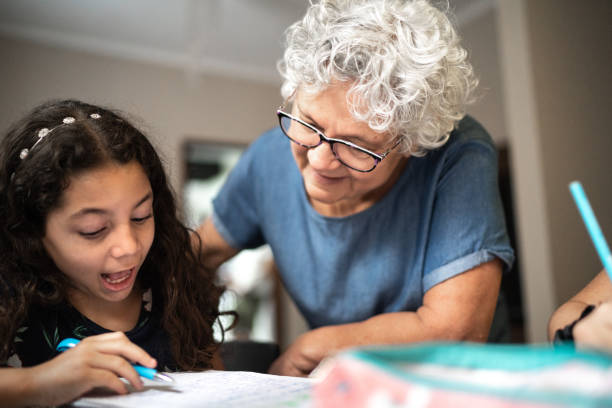 grandmother helping granddaughter with homework while he's studying at home - grandparent reading grandmother child imagens e fotografias de stock