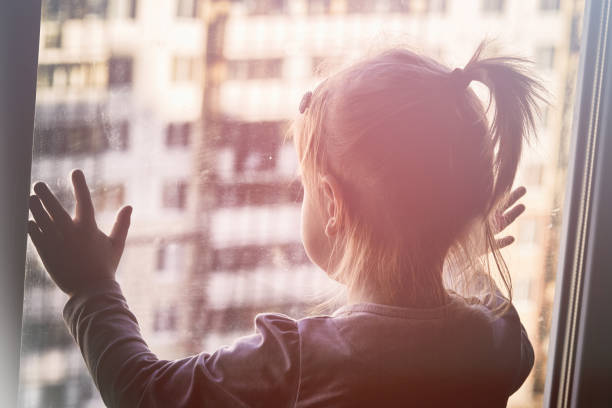 istock Girl looks lonely through window by putting her hands on window sill 1249654293