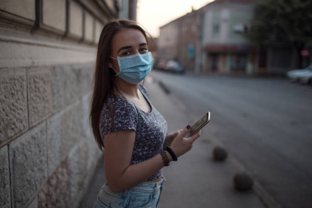 istock Beautiful woman using mobile phone with protective mask on street 1249659371