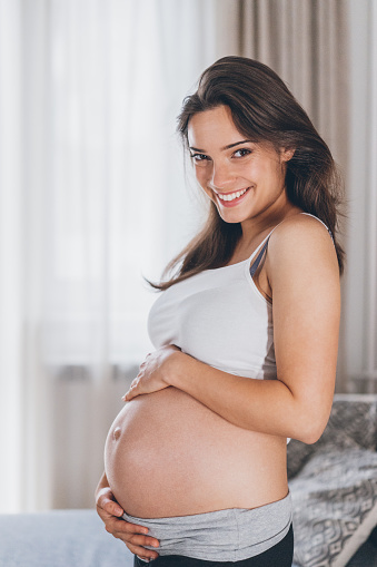 Beautiful young woman touching her pregnant belly at home