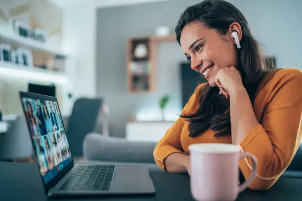 Young and beautiful woman having video online meeting using her laptop and Wireless earbuds at home