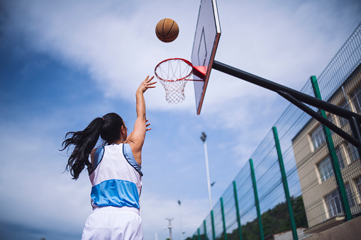 Rear view of woman aiming at basketball hoop.