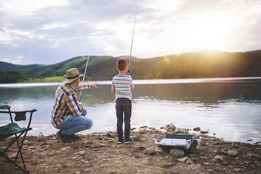 Father and son fishing at sunset in beautiful mountain lake.