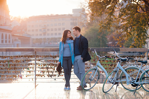 Young couple in love standing on bridge in sunset and looking happy.