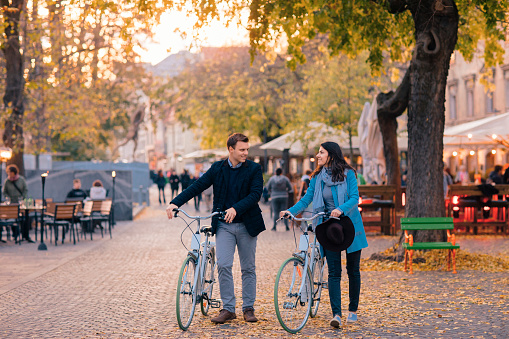 Happy smiling couple riding a bike in old European town on autumn day and looking at each other.