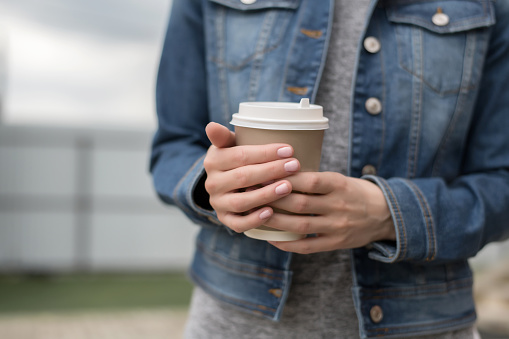 Women's hands in a denim jacket hold a Cup of coffee.