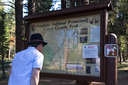 Los Alamos, NM: A man reading an Information sign with a trail map at Bandelier National Monument near Los Alamos.