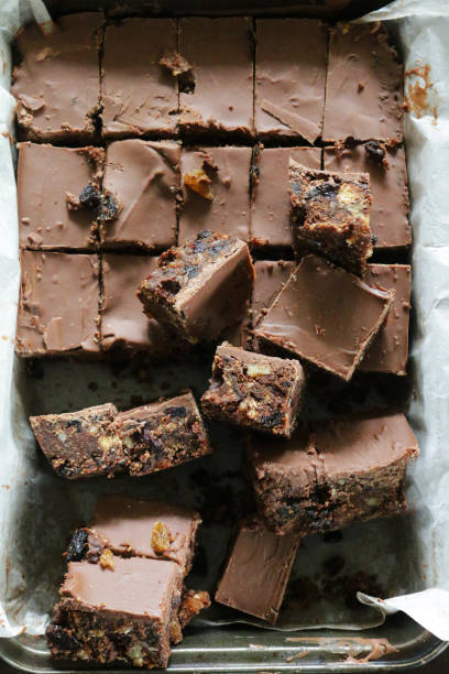 Stock photo of close-up of homemade fridge cake recipe, no bake chocolate tiffin cake made with biscuits, dried fruits, nuts and egg with a layer of melted milk chocolate, tray bake cakes snack cut into squares, in stack pile, on blue plate primer plano de la receta casera de pastel de nevera, sin pastel de tiffin de chocolate al horno hecho con galletas, frutos secos, nueces y huevo con una capa de chocolate con leche derretida, bandeja hornear pasteles merienda cortada en cuadrados, en pila