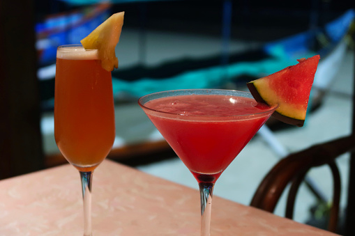 Stock photo showing cocktail drinks on the table, Sex on the Beach orange and vodka based alcoholic cocktail, and cosmopolitan cocktail  of vodka, cranberry, orange liqueur with a slice of watermelon stood on a wooden table in an Indian restaurant. Non-alcoholic versions of cocktails are often referred to as mocktails.