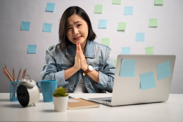 asiatische frau hält hände im gebet, die in die kamera schaut und arbeitet an einem laptop im home office. wfh. arbeiten sie von zu hause aus. prävention coronavirus covid-19 konzept. - pleading women business sadness stock-fotos und bilder