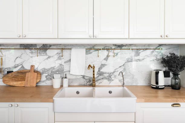 istock Modern classic kitchen interior with kitchen appliances and white ceramic sink with gold mirror faucet on wood top with marble wall in the background / kitchen interior 1249711148