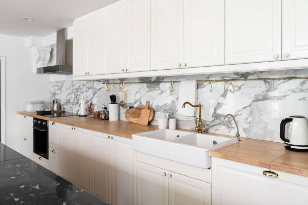 istock Modern classic kitchen interior with kitchen appliances and white ceramic sink with gold mirror faucet on wood top with marble wall in the background / kitchen interior 1249711149