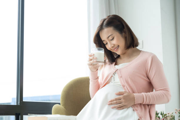 joven embarazada con vaso de leche en la habitación - mujer bebiendo leche fotografías e imágenes de stock