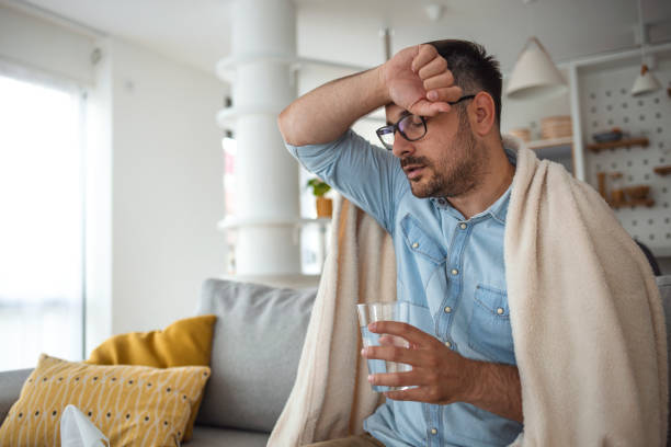 Ill man covered with blanket. Cropped shot of a young man suffering with flu while sitting wrapped in a blanket on the sofa at home. It's the season of sneezes. Ill man covered with blanket. man fever stock pictures, royalty-free photos & images