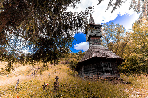 Wide angle color image depicting a small orthodox church in the middle of the countryside in Transylvania, Romania. The little church is surrounded by lush green meadows and rolling hills. Room for copy space.
