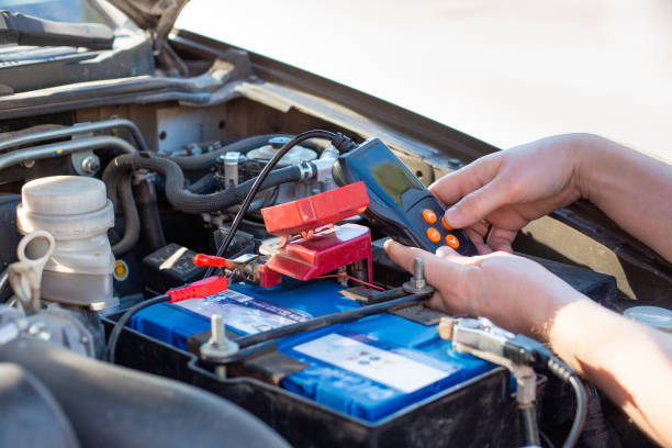 un meccanico di auto sotto il cofano di un'auto diagnostica una batteria di un'auto con un tester, riparazione e sostituzione della batteria - battery replacement foto e immagini stock
