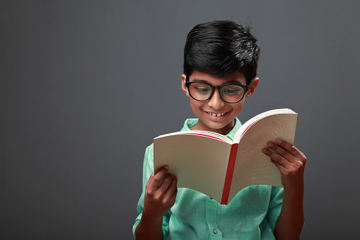 Little boy wearing spectacles reads a book