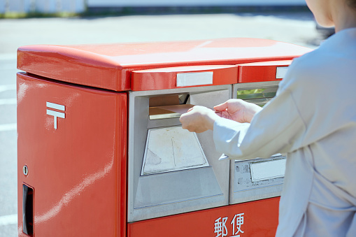 Hand of a young woman putting an envelope in a post box