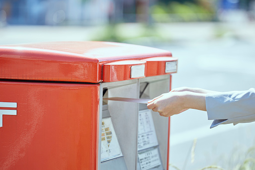 Hand of a young woman putting an envelope in a post box
