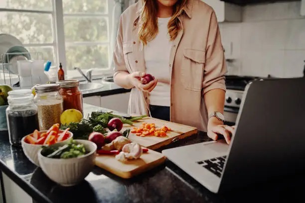 Photo of Young female blogger searching online browsing for recipes to prepare salad of fresh vegetables and post on social media in vlog - new hobby during isolation
