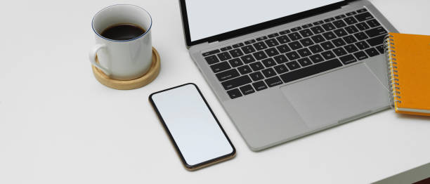 istock Modern worktable with blank screen smartphone, laptop and coffee cup on white desk 1249733490
