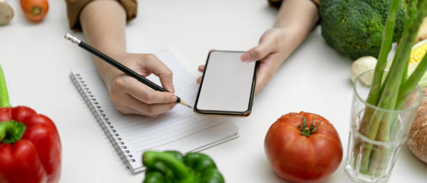 istock Female taking recipe notes on blank notebook while looking informations on mock-up smartphone 1249733579