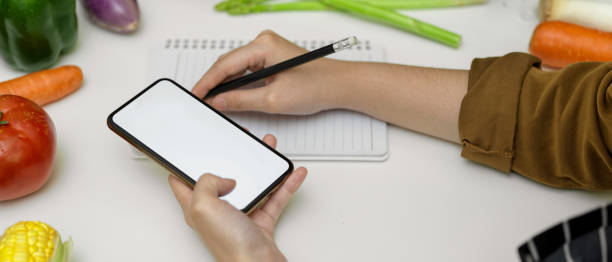 istock Female taking recipe notes on blank notebook while looking informations on mock-up smartphone 1249733780