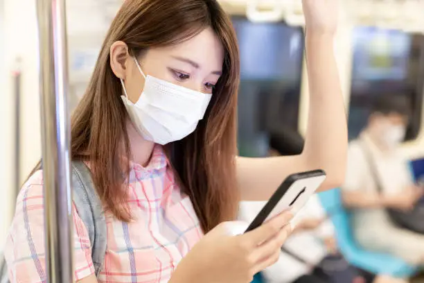 College girl use mobilephone when commute on mrt and wear face mask