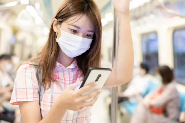 College girl use mobilephone when commute on mrt and wear face mask