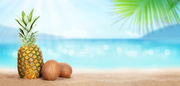 Summer tropical sea with sparkling waves, pineapple and coconuts on hot sand beach. Travel and vacation concept with copy space