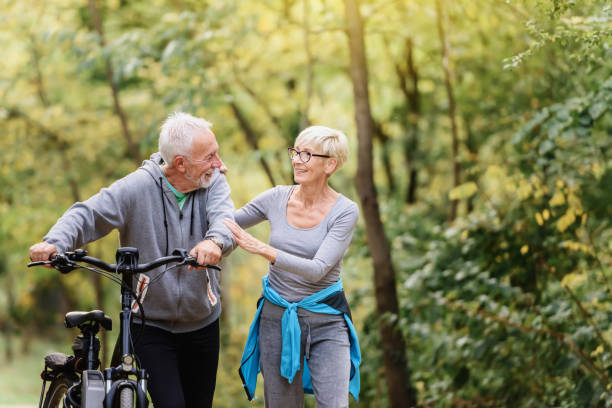 istock Cheerful active senior couple with bicycles walking through park together 1249745085
