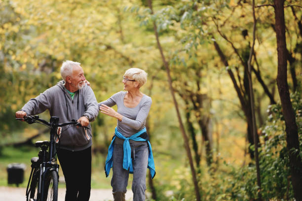 istock Cheerful active senior couple with bicycles walking through park together 1249745469