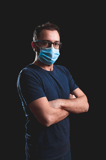 Adult person with protective face mask posing on a black background - social issues with virus and hygiene safety measures.
