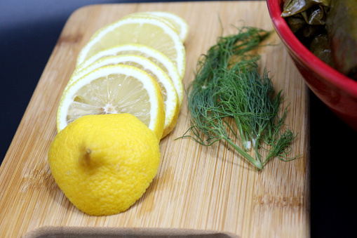 Side dish with lemon slices and dill near to cooked meal plate