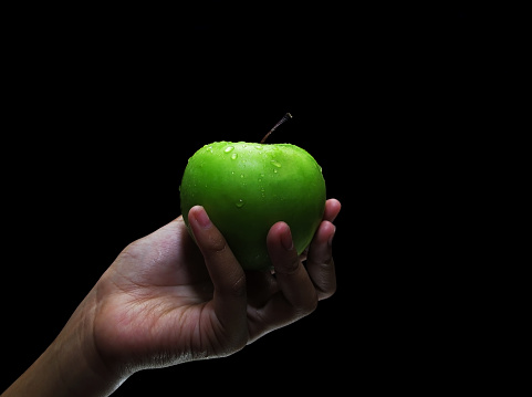woman's hand holding an apple with a black background