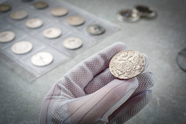 numismatics. old collectible coins made of silver on a wooden table.  a collector in special gloves holds an old coin. - coin collection imagens e fotografias de stock