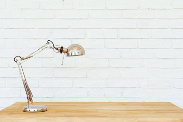 Modern home office with lamp on wooden table and white brick wall background.