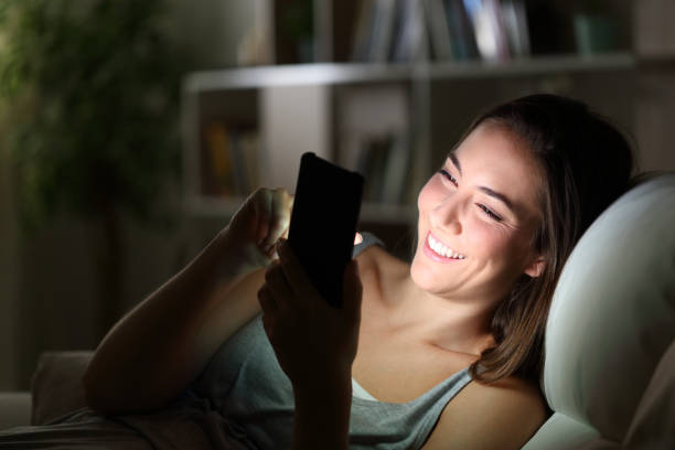 счастливая женщина, используя телефон ночью с облегченный лицо - lightened стоковые фото и изображения