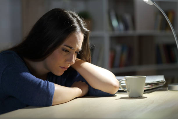 mulher triste reclama de sentar em uma mesa à noite em casa - teenager dark pensive emotional stress - fotografias e filmes do acervo