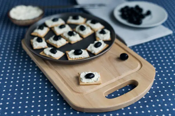 Photo of Plate with crackers with soft cheese and olives on a blue polka dot tablecloth.