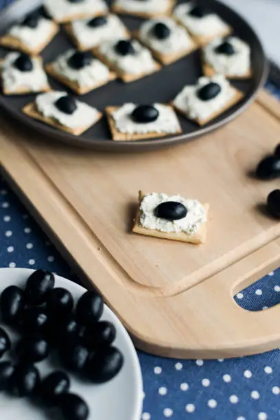 Photo of Plate with crackers with soft cheese and olives on a blue polka dot tablecloth.