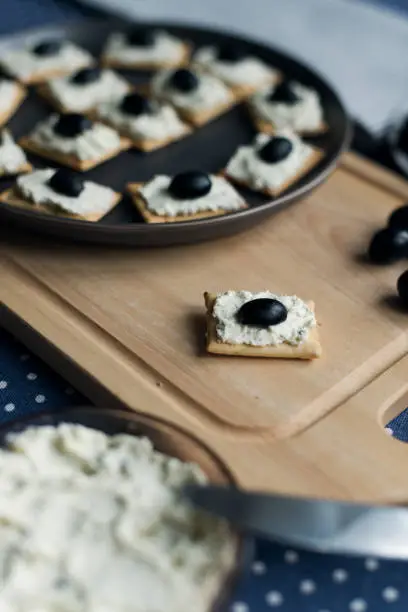 Photo of Plate with crackers with soft cheese and olives on a blue polka dot tablecloth.