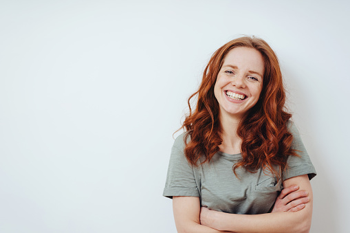 Relaxed confident friendly young woman in a casual T-shirt standing with folded arms in front of a white wall with copy space