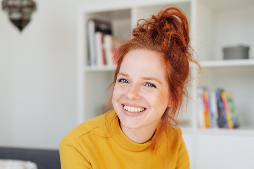 Close-up front portrait of a beautiful young woman in yellow with red hair, looking at camera with friendly face and laughing or smiling