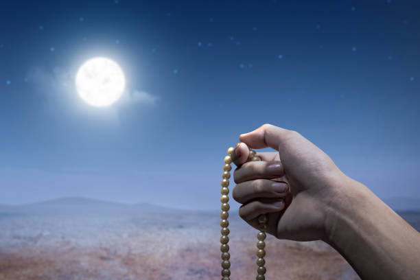 Muslim man praying with prayer beads on his hands with a night scene background