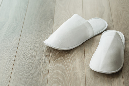 Copy space shot of pair of nice, cozy, simple white slippers for spa on a wooden floor.
