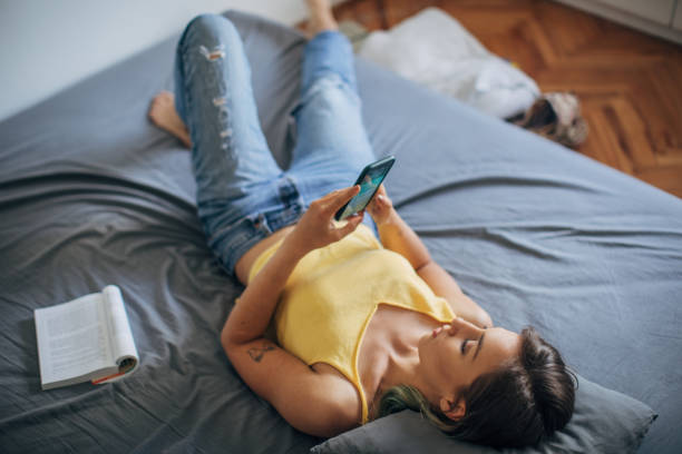 istock Young woman lying on her bed and using smart phone 1249768051